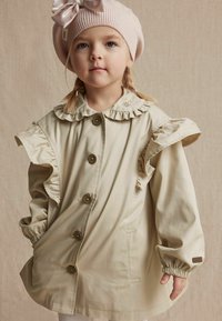 Beige gerimpelde jas met knoopsluiting, voorzien van een gefronste kraag en elastische mouwen. Vergezeld van een lichtroze gebreide baret.
