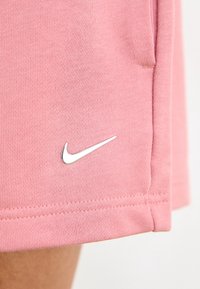 Růžové Nike šortky vyrobené z texturovaného materiálu s úzkým střihem. Mají stříbrné logo Nike swoosh poblíž lemu a boční kapsu.