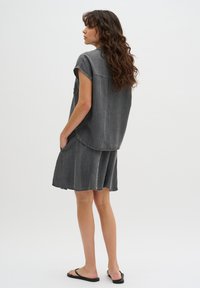 Abito in denim grigio con maniche corte, corpino aderente e gonna ampia. Presenta tasche laterali e un orlo curvo. Indossato con sandali neri.