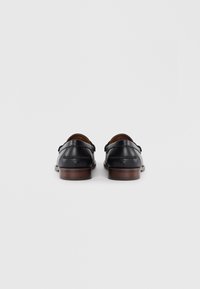 Zapatos de cuero negro con un acabado suave, que cuentan con un pequeño tacón y costura decorativa en la parte trasera. Suela de madera.
