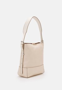 Sac à main en cuir beige avec une texture lisse, de forme verticale, une bandoulière réglable et des ferrures en ton argent. Fines coutures discrètes à la base.