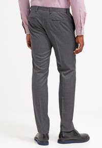 Graue strukturierte Anzughose mit schmaler Passform, ausgestattet mit zwei Gesäßtaschen und einem glatten Bund, kombiniert mit schwarzen Schuhen.