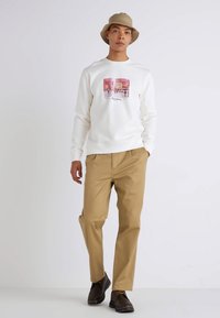 Sweatshirt blanc avec un motif sur le devant, associé à un pantalon beige clair. Chaussures noires avec des lacets jaunes. Texture lisse et coupe décontractée.