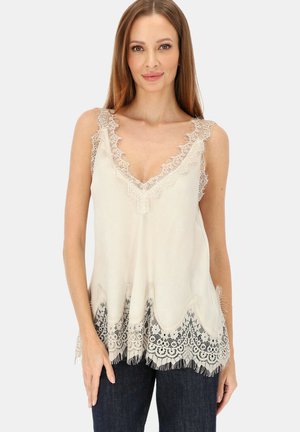 Kremowy, bezrękawnik z głębokim dekoltem w kształcie litery V, ozdobiony misterną koronką, falistym dołem i frędzlami u podstawy, uzupełniony przezroczystą teksturą.