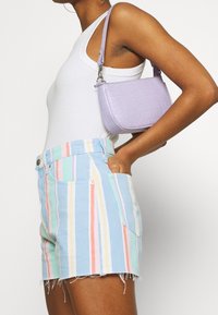 Pantalones cortos de mezclilla a rayas en azul claro, rosa, verde y amarillo con dobladillos deshilachados, combinados con un pequeño bolso de mano lavanda con textura de cocodrilo.