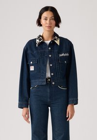 Denim jacket with a dark blue finish, cow-patterned collar, front pockets, and embroidery. Cropped design with silver hardware accents.