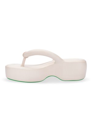 Sandalia flip-flop de plataforma en un beige claro con una suela gruesa y redondeada y un acento verde elevado. La correa presenta un diseño curvado y suave.