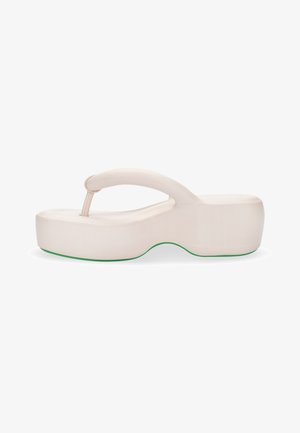 Tongs plates enbeige clair avec une semelle épaisse et arrondie, et un accent vert surélevé. La sangle présente un design doux et courbé.