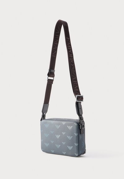 Ορθογώνια γκρι τσάντα ώμου με επαναλαμβανόμενο λογότυπο αετού και ρυθμιζόμενο σκούρο καφέ λουρί με την επιγραφή "EMPORIO ARMANI".