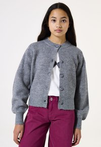 Grauer Strickcardigan mit gerippter Textur, rundem Halsausschnitt und fünf Knöpfen. Kombiniert mit hoch taillierten, tiefrosa Hosen.