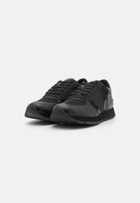 Scarpe da ginnastica nere realizzate con una combinazione di pelle texturizzata e mesh. Presentano una forma arrotondata, lacci frontali e una suola spessa in gomma a contrasto.