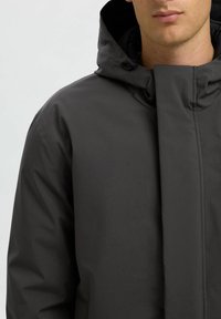 Giacca nera impermeabile con colletto alto, dettagli di cucitura multipla e cappuccio regolabile con tirante per una vestibilità personalizzata.
