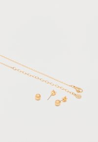 Λεπτή χρυσή αλυσίδα κολιέ με δύο μικρά σφαιρικά χρυσά σκουλαρίκια καρφάκια σε λευκό φόντο.