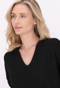 Maglione nero aV con lavorazione morbida e finitura testurizzata, con maniche corte e vestibilità rilassata. Orecchini a cerchio dorati aggiungono un tocco di stile.