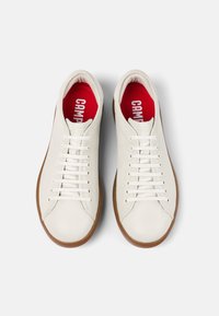 Valged nahast jooksujalatsid sujuva tekstuuriga, ümarate vormidega ja pruunide kummitaldadega. Punased jalatsisisud esitavad "CAMPER" brändimist.