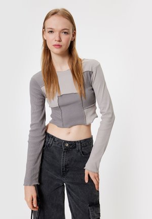 Gray cropped long-sleeve top with ribbed texture, featuring contrasting patch design. Paired with high-waisted black cargo pants.