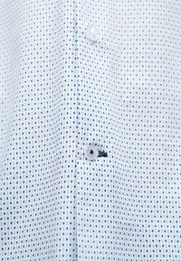 Λευκό πουκάμισο με σχέδιο από μικρά μπλε διαμαντένια σχήματα και ορατά διάφανα λευκά κουμπιά κατά μήκος του πέτο.