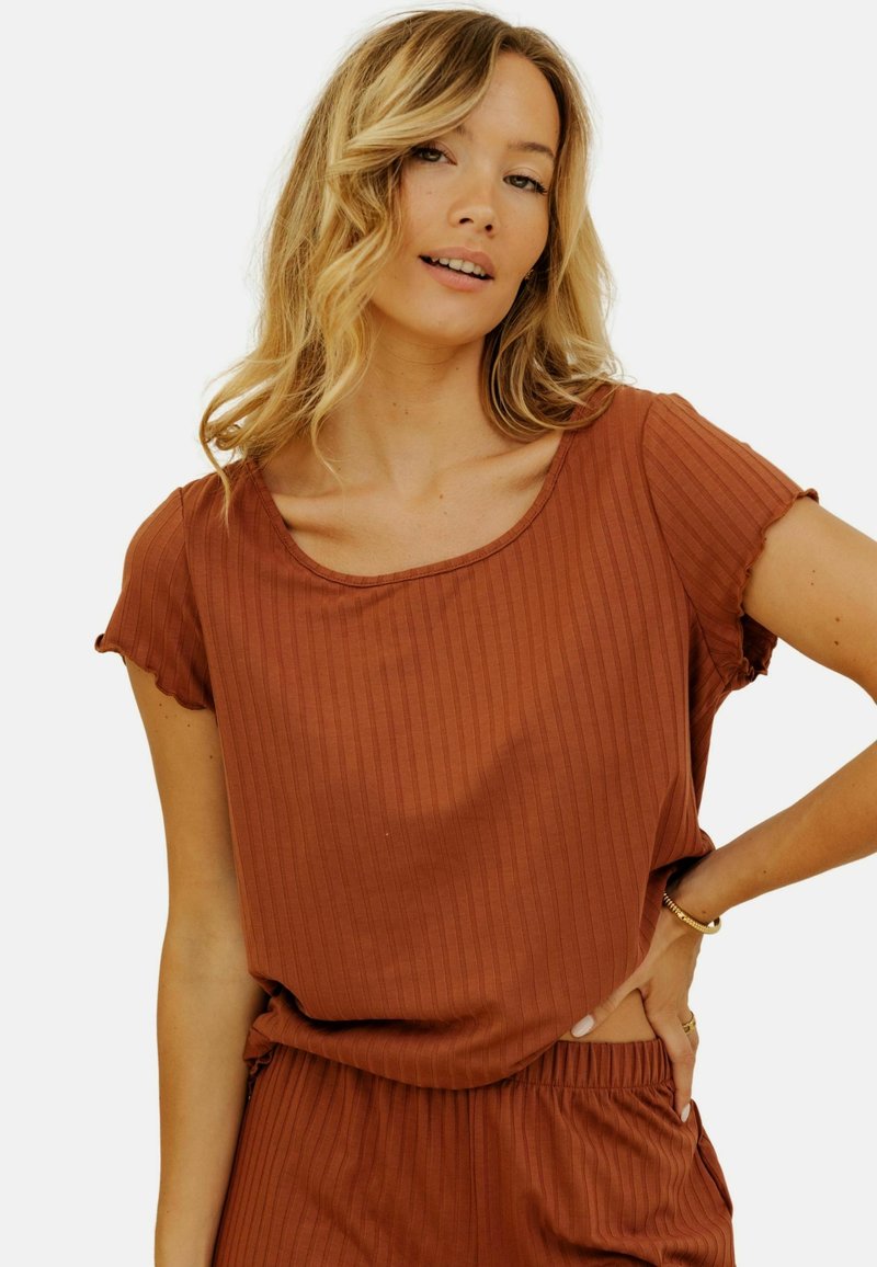 Un haut côtelé de couleur rouille avec un décolleté arrondi et de courtes manches volantes. Le tissu semble doux avec un léger éclat, associé à un short assorti.