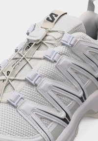 Αθλητικό παπούτσι ανοιχτού γκρι με ύφασμα από δίχτυ, ρυθμιζόμενο σύστημα γρήγορου δέσιμου κορδονιών και καλουπωμένες επικαλύψεις πλευρών για στήριξη.