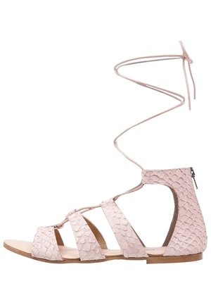 Light pink sandal with a textured, reptile-like design, multiple straps, and a back zipper. Includes a laced ankle tie for secure fastening.