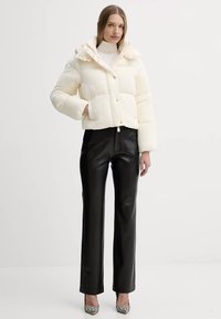 Giacca puffer crema con cappuccio, caratterizzata da un design trapuntato e bottoni dorati, abbinata a pantaloni in pelle nera a vita alta e scarpe con tacco a fantasia.