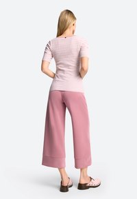 Gestreifter, körperbetonter Oberteil in Rosa und Weiß, kombiniert mit weiten rosa Hosen und rosa Clogs mit Nietenakzenten. Angenehme Stoffstruktur insgesamt.