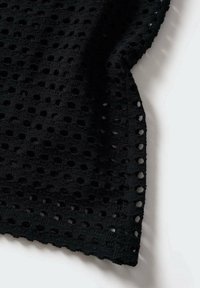 Tissu tricoté noir avec un motif texturé à trous ouverts, offrant une belle tombée et un bord lisse, mettant en valeur des détails de design sophistiqués.