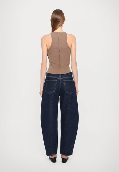 Braunes, tailliertes Tanktop mit einer Rückennaht, kombiniert mit blauen, weit geschnittenen Denim-Jeans mit Rückentaschen und einer dunklen Waschung.