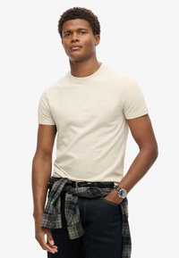 Beige bomulds t-shirt med rund hals og korte ærmer, der har et lille, diskret logo. Casual stil kombineret med en ternet skjorte om livet.