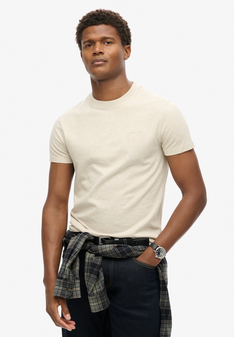 Beige bomulds t-shirt med rund hals og korte ærmer, der har et lille, diskret logo. Casual stil kombineret med en ternet skjorte om livet.