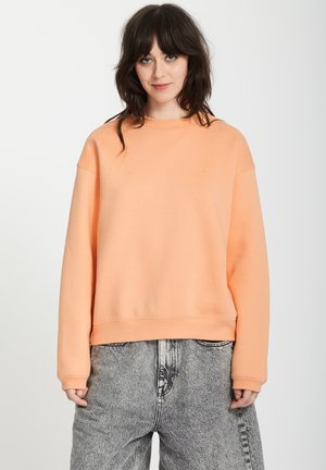 Pfirsichfarbener Sweatshirt mit Rundhalsausschnitt, gerippten Bündchen und Saum. Verfügt über ein kleines Logo auf der Brust und eine lockere Passform. Kombiniert mit grauen gemusterten Hosen.