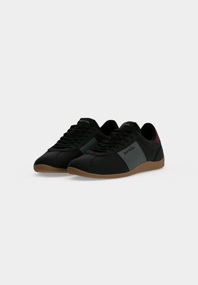 Paire de baskets noires à lacets avec des panneaux latéraux gris, des semelles marron et un marquage discret sur le côté et la languette.