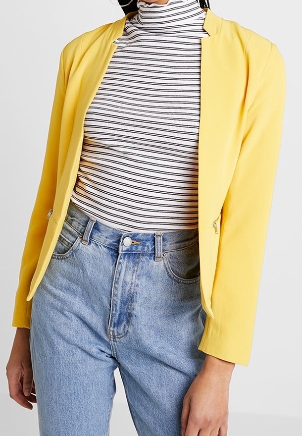Blazer léger jaune au design simple, assorti à un col roulé à rayures noires et blanches et un jean bleu taille haute.