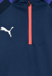 Mornarska atletska jakna od teksturirane tkanine s kratkim crvenim zatvaračem. Ima bijeli Puma logo i ljubičaste akcentne detalje na ramenima.