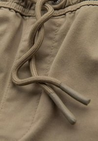 Cordons en khaki avec texture tressée sur un tissu léger. Les coutures sont visibles le long de l'ourlet, indiquant une construction durable.