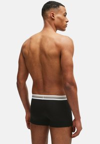 Svarta boxerfilmer med en vit randig midjeband, visad från baksidan. Materialet verkar mjukt med en slät textur.