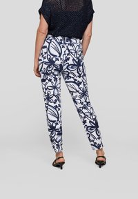 Fitted trousers with a white background and navy floral pattern. Smooth fabric, tapered legs, and a standard waist. Worn with black heeled sandals.