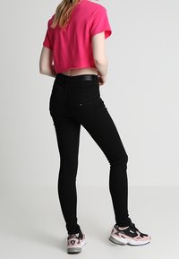 Jeans ajustados negros de cintura alta, combinados con una camiseta corta rosa y zapatillas rosas y negras. Textura suave y minimalismo en los detalles.