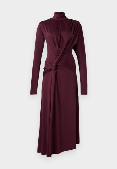Vestido de manga longa e gola alta em tecido bordeaux profundo. Apresenta um detalhe de nó na cintura e uma saia fluida que se estende até ao chão.