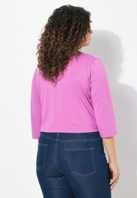 Haut long à manches courtes de couleur violette avec un col rond, associé à un jean en denim bleu foncé avec poches arrière et coutures contrastantes.