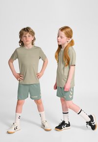 Barnidrottskläder med ljusgröna kortärmade tröjor, matchande shorts med vita detaljer och omatchande svartvita skor.