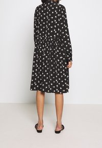 Svart långärmad klänning med blommönster, med en indragen midja och en utsvängd kjol. Mjukt material, knälång med en avslappnad passform.