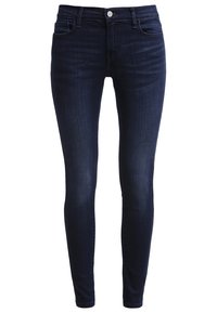 Jean skinny bleu foncé avec fermeture avant par bouton et zip, poches avant et arrière, et détails subtilement délavés.