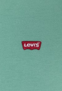 Petite étiquette rouge avec le logo Levi's cousue sur un tissu tricoté bleu sarcelle clair.