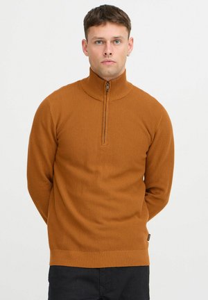 Brown zip-up sweater featuring a textured knit design, high collar, and ribbed cuffs, paired with dark trousers.