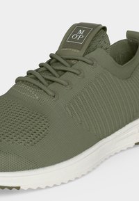 Baskets en maille vert olive avec semelle blanche, design lacé, et étiquette de marque sur la languette indiquant "M OP."