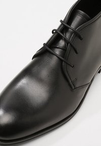 Černé kožené společenské boty s hladkým povrchem, zaoblenou špičkou a třemi očky pro šněrování. Obsahují jemné švy.