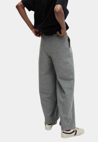 Grijze Baumwoll-Sweatpants mit lockerem Schnitt, Seitentaschen und elastischem Bund, kombiniert mit weißen Sneakern mit marineblauen Akzenten.