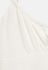Tissu blanc avec un détail élastique froncé, probablement partie d’un vêtement comme une manche ou un décolleté, montré en gros plan.