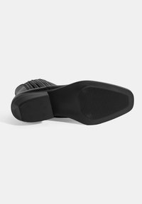 Bottines noires avec une tige texturée ornée de rayures verticales, un bout arrondi et une semelle plate en caoutchouc avec des rainures horizontales.